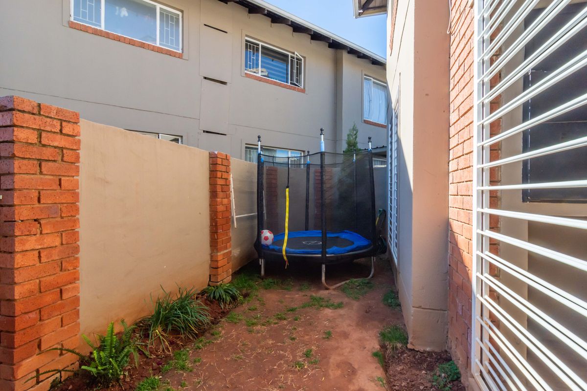A narrow rear courtyard area featuring brick boundary walls and security-fitted windows, providing a private outdoor space for the apartment.