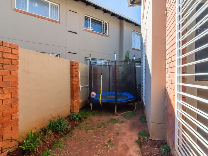 A narrow rear courtyard area featuring brick boundary walls and security-fitted windows, providing a private outdoor space for the apartment.