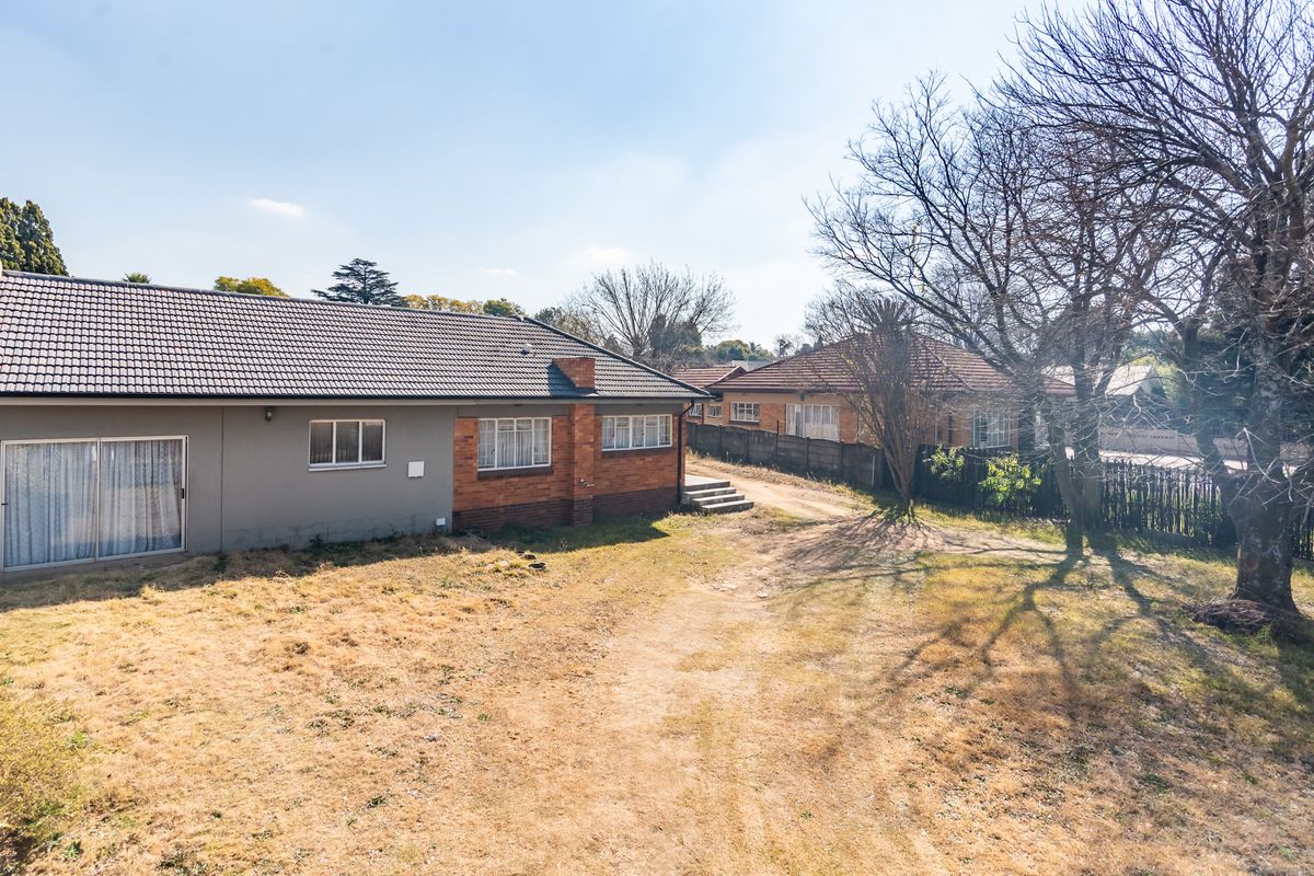 Rear view of the property featuring a brick and rendered facade, tiled roof, and a large backyard area with established trees.