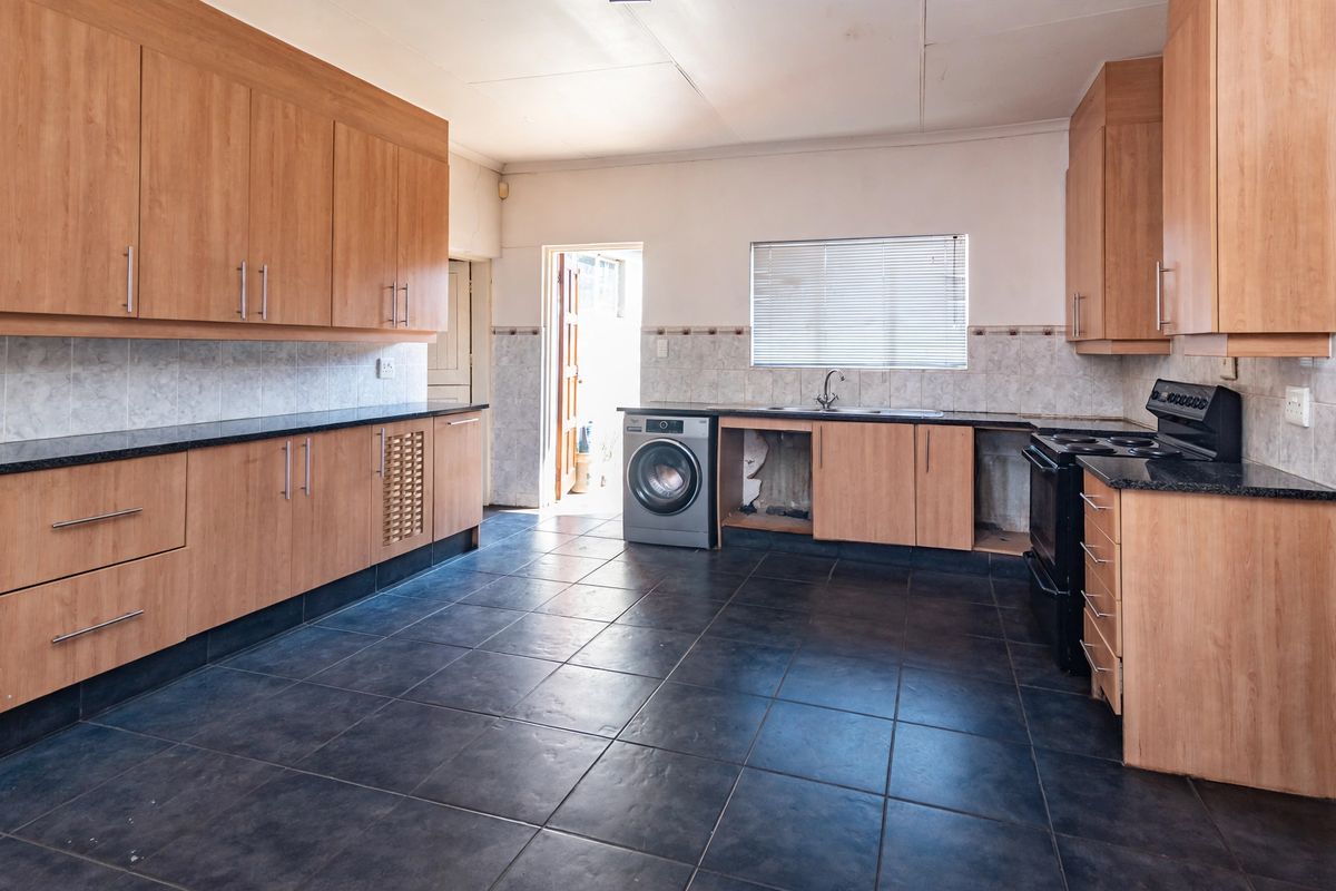 Spacious kitchen featuring laminate cabinetry, granite countertops, and dark tiled flooring, offering a functional layout with potential for modern updates.