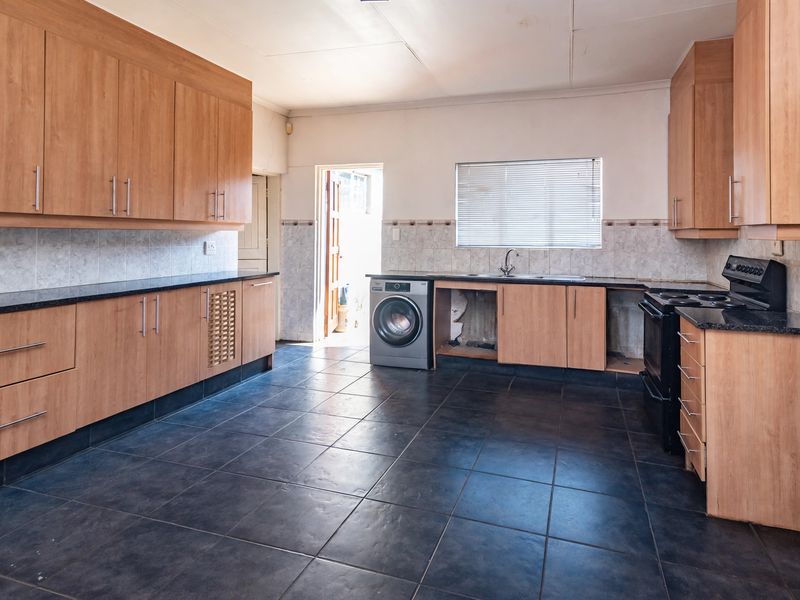 Spacious kitchen featuring laminate cabinetry, granite countertops, and dark tiled flooring, offering a functional layout with potential for modern updates.