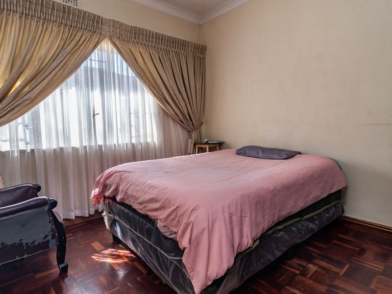 A bedroom featuring classic parquet flooring, neutral wall finishes, and large windows with existing curtain tracks, offering a solid foundation for modernization.