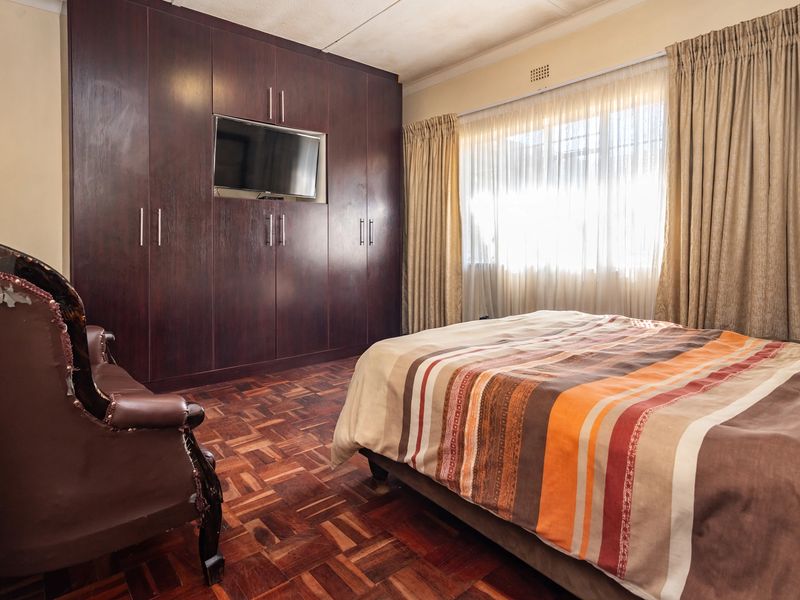 A bedroom featuring dark wood built-in cupboards, classic parquet flooring, and large windows with curtain rails, offering a functional and traditional living space.