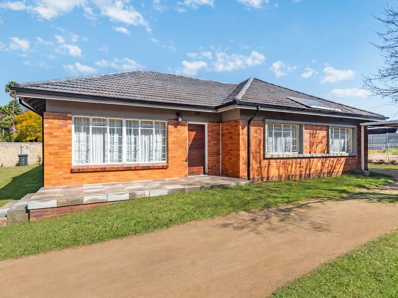 A single-story brick house featuring a tiled roof, solar water heater, and a paved entrance porch, set on a spacious grassed lot.