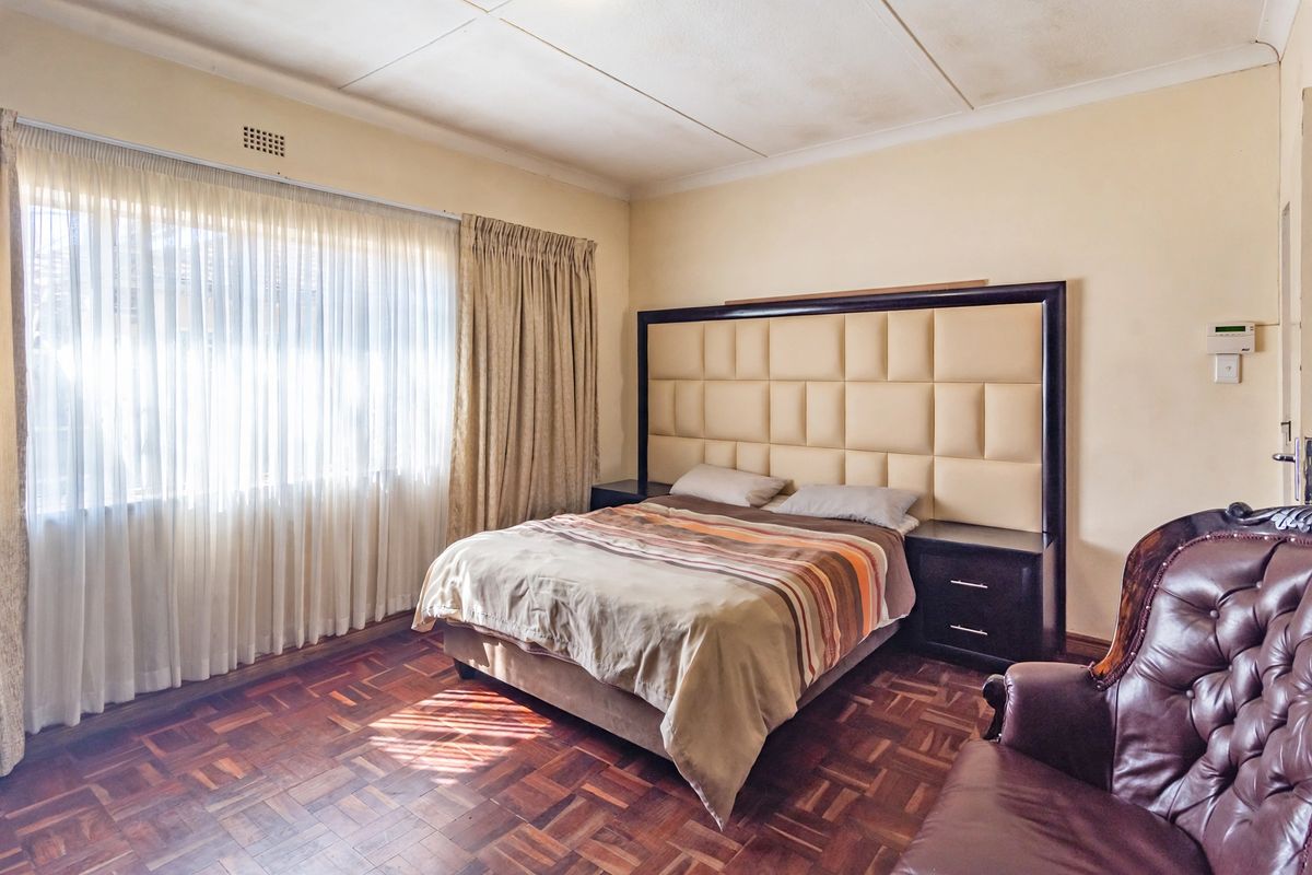 A bedroom featuring classic parquet flooring, a large built-in headboard with integrated bedside tables, and natural light through large windows.