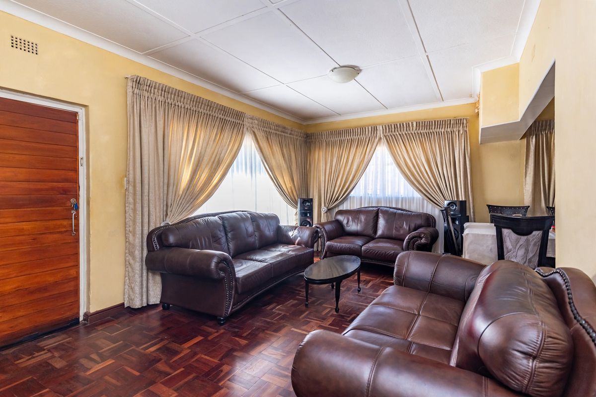 A living room featuring classic parquet flooring, a solid timber door, and neutral wall finishes, offering a traditional layout with ample natural light.