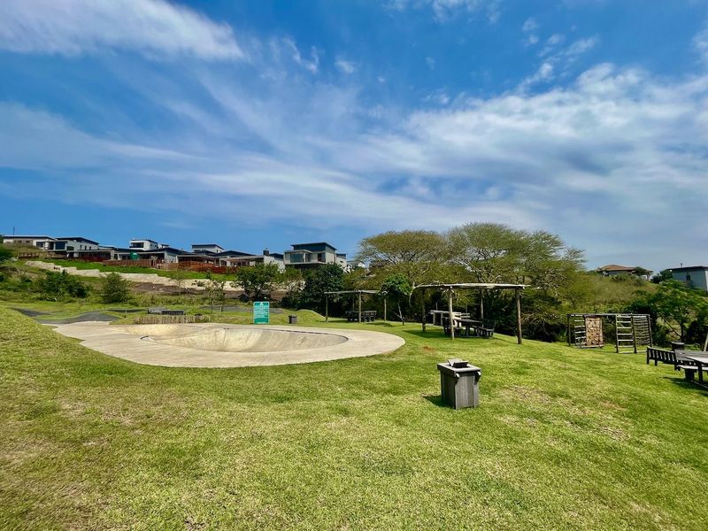 A well-maintained communal garden area featuring a concrete skate bowl, timber pergola, and outdoor climbing equipment set within a residential estate.