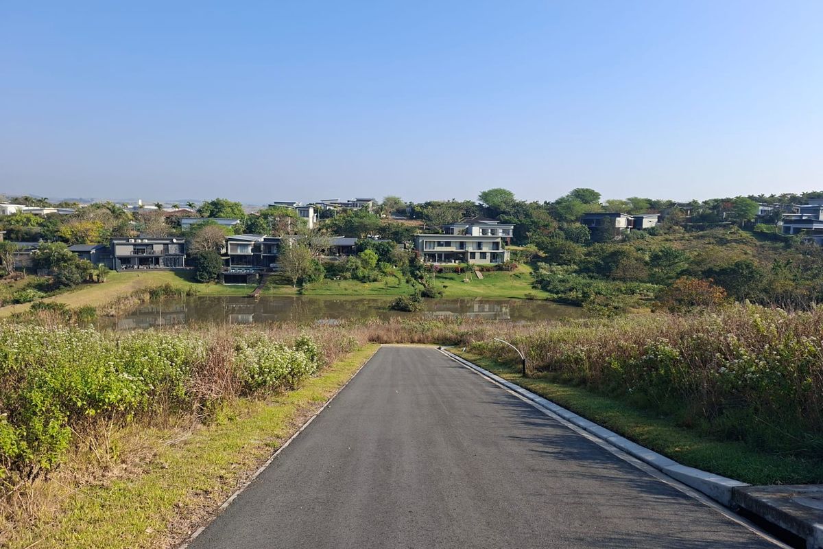 A scenic view overlooking a residential estate with a central pond, featuring a paved access road and established landscaping.