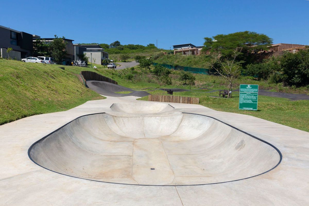 A well-maintained outdoor concrete skate bowl and asphalt pump track situated within a residential estate's recreational area.