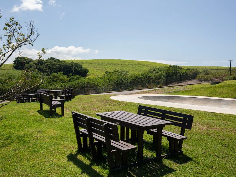 A well-maintained outdoor garden area featuring a concrete skate bowl, manicured lawn, and scenic hillside views.