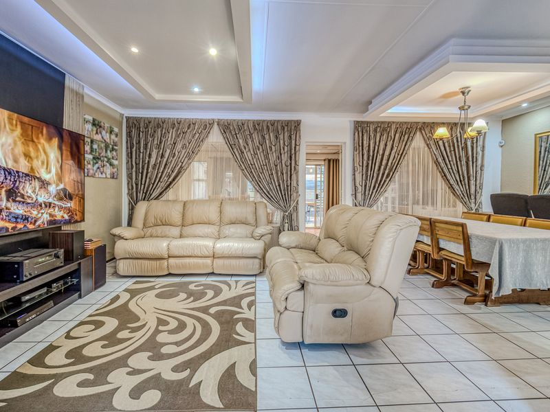 Spacious open-plan living and dining area featuring tiled flooring, recessed ceilings with integrated lighting, and a modern entertainment wall.