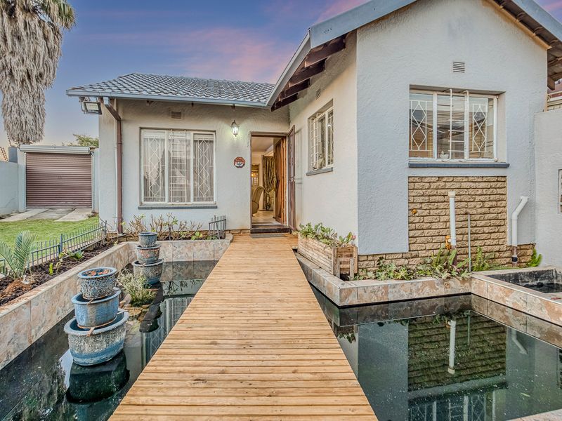Front entrance featuring a timber walkway over a water feature, leading to a home with a tiled roof and security-barred windows.