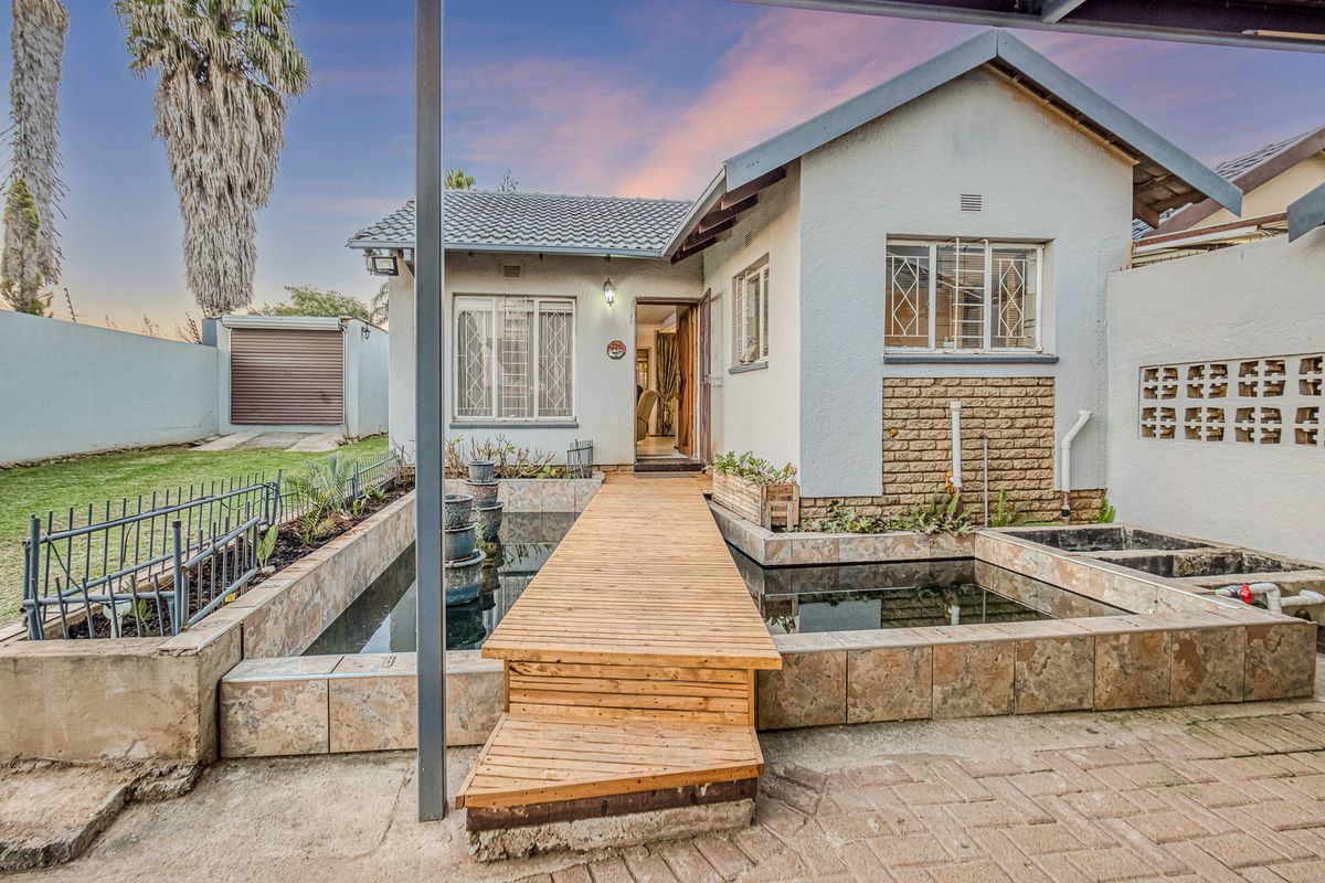 Rear exterior view featuring a wooden deck walkway over a water feature, brick and stone facade, and paved patio area.