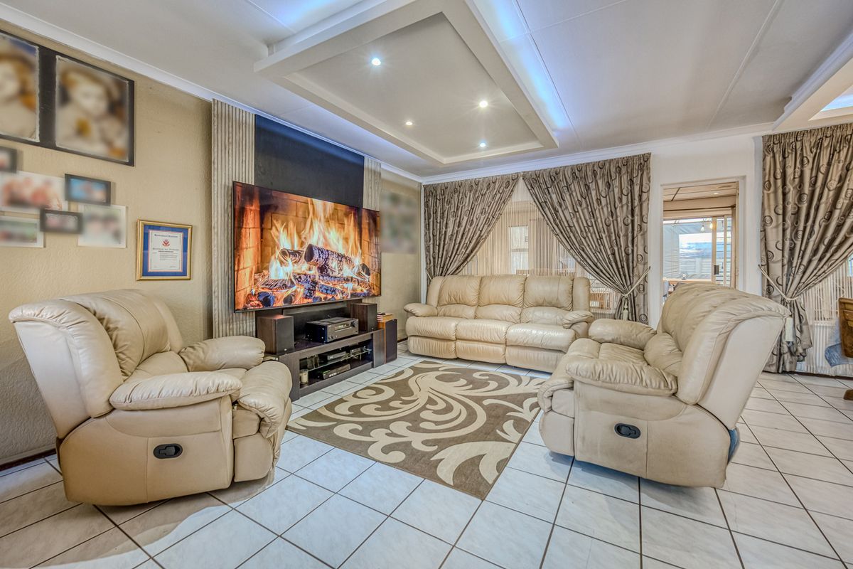 A well-maintained living room featuring tiled flooring, a decorative recessed ceiling with integrated downlights, and a dedicated media wall area.