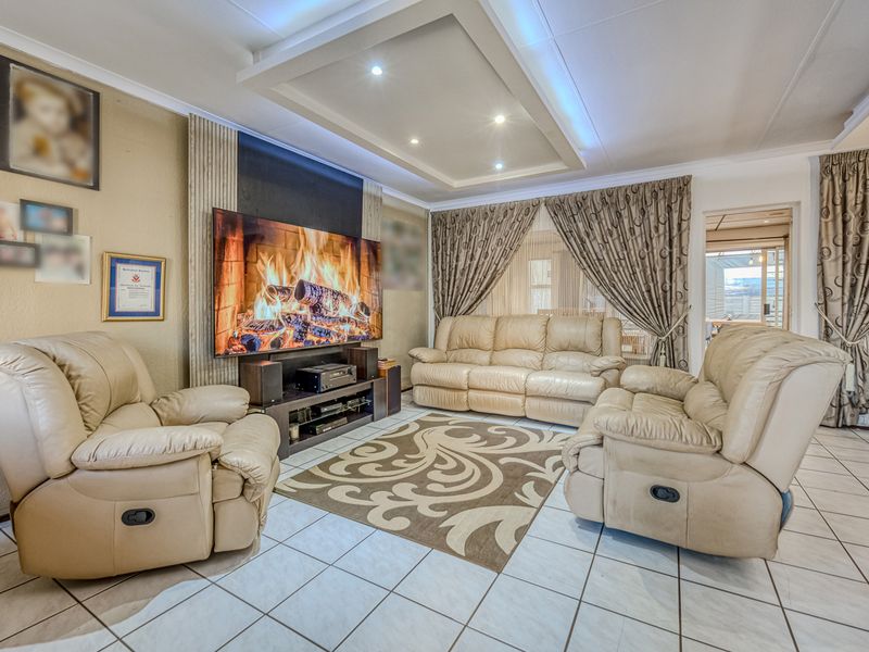 A well-maintained living room featuring tiled flooring, a decorative recessed ceiling with integrated downlights, and a dedicated media wall area.