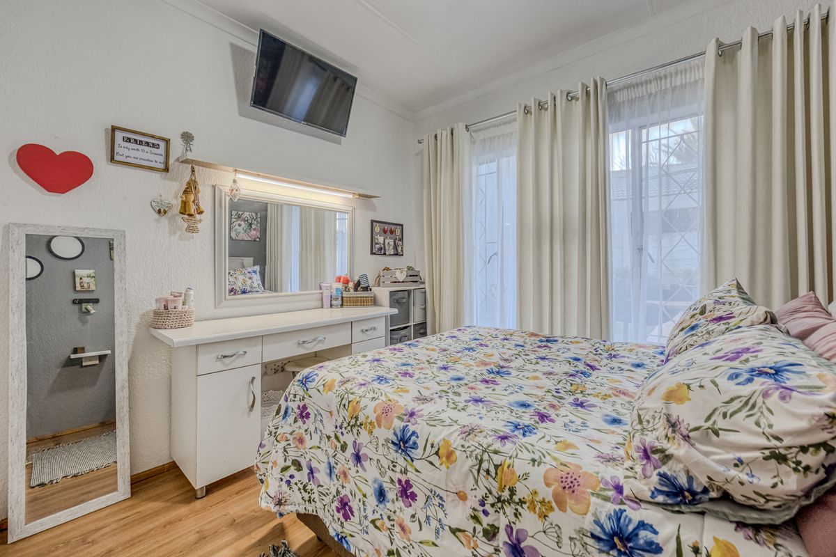 A well-lit bedroom featuring laminate flooring, a built-in vanity, and sliding glass doors with security gates providing access to the exterior.