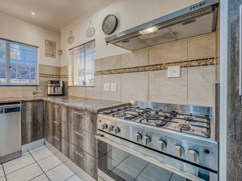 A functional kitchen featuring wood-look cabinetry, stone-effect countertops, a gas stove with extractor fan, and tiled flooring.