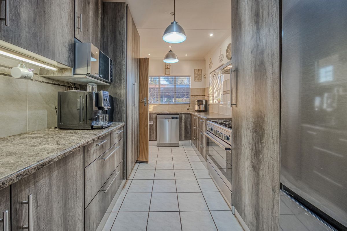 Modern galley-style kitchen featuring wood-look laminate cabinetry, granite countertops, stainless steel appliances, and tiled flooring with ample storage space.