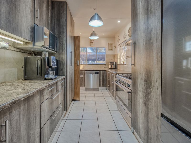 Modern galley-style kitchen featuring wood-look laminate cabinetry, granite countertops, stainless steel appliances, and tiled flooring with ample storage space.
