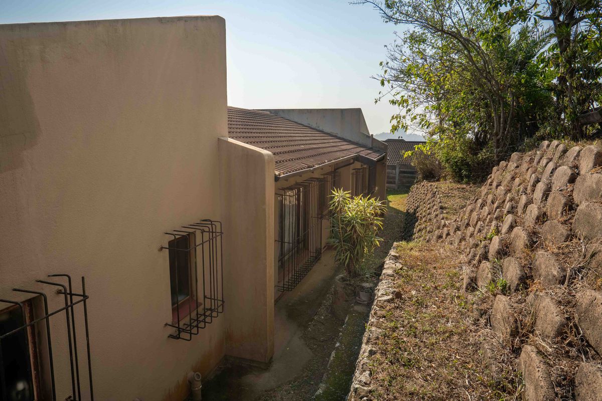 Rear exterior view of the property featuring a tiled roof, security bars on windows, and a stone retaining wall along the side path.
