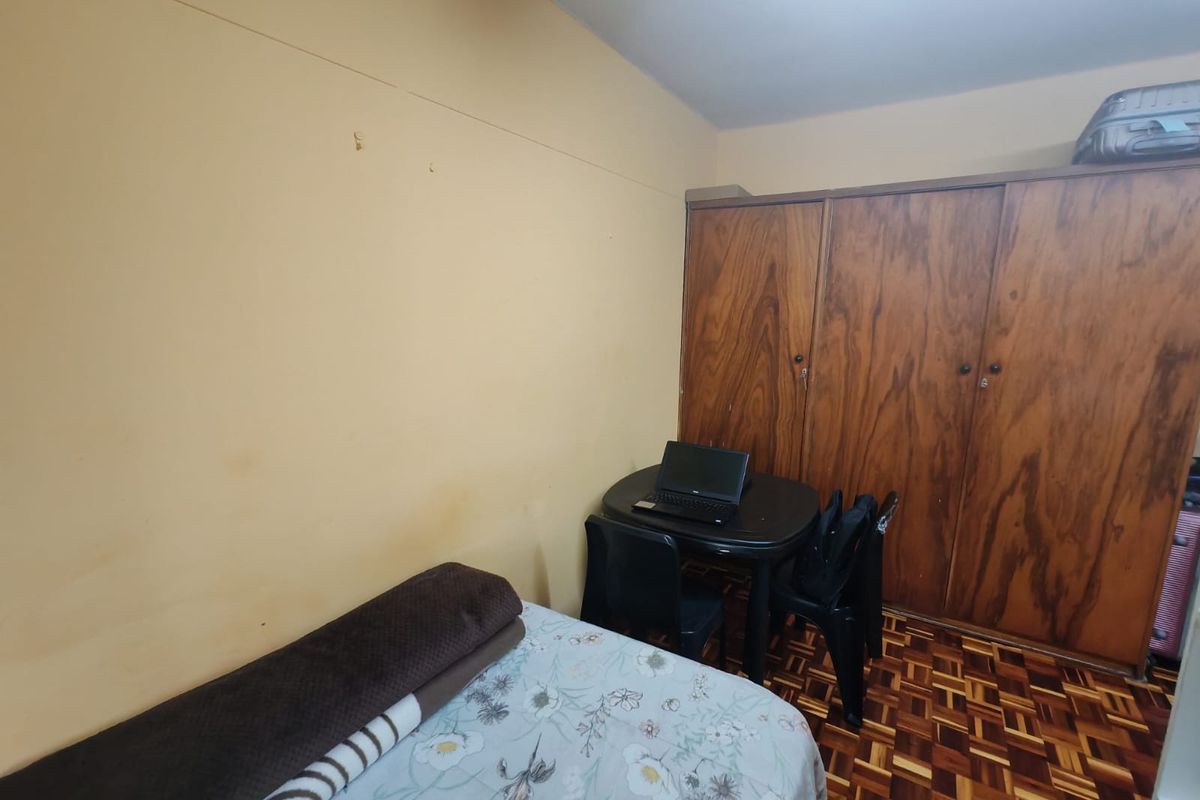 A bedroom featuring classic parquet flooring and a large built-in wooden wardrobe, offering functional storage space in a compact layout.