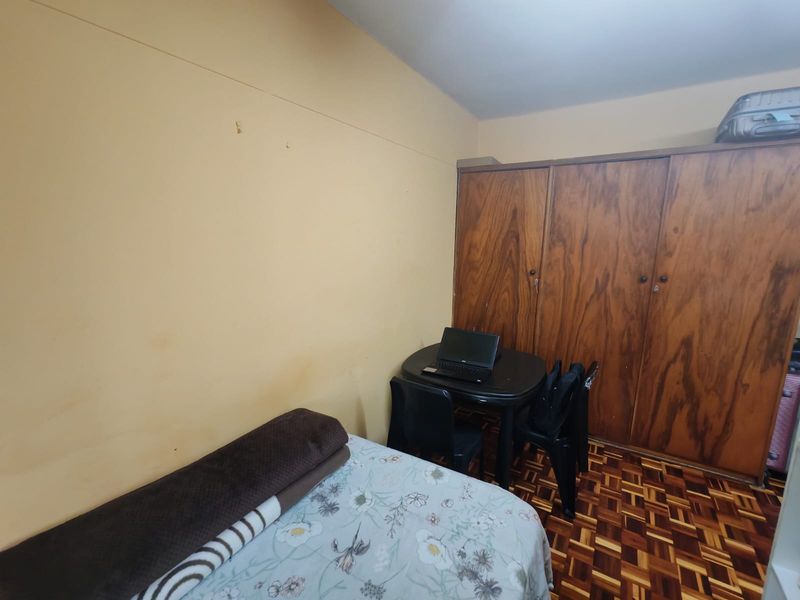 A bedroom featuring classic parquet flooring and a large built-in wooden wardrobe, offering functional storage space in a compact layout.