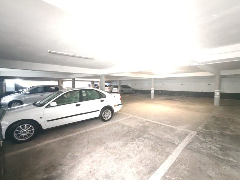 A covered basement parking garage featuring concrete flooring, support columns, and overhead fluorescent lighting.