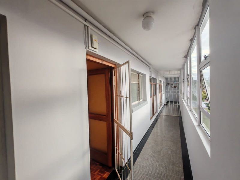 A functional apartment hallway featuring tiled flooring, security gates, and large windows providing natural light.