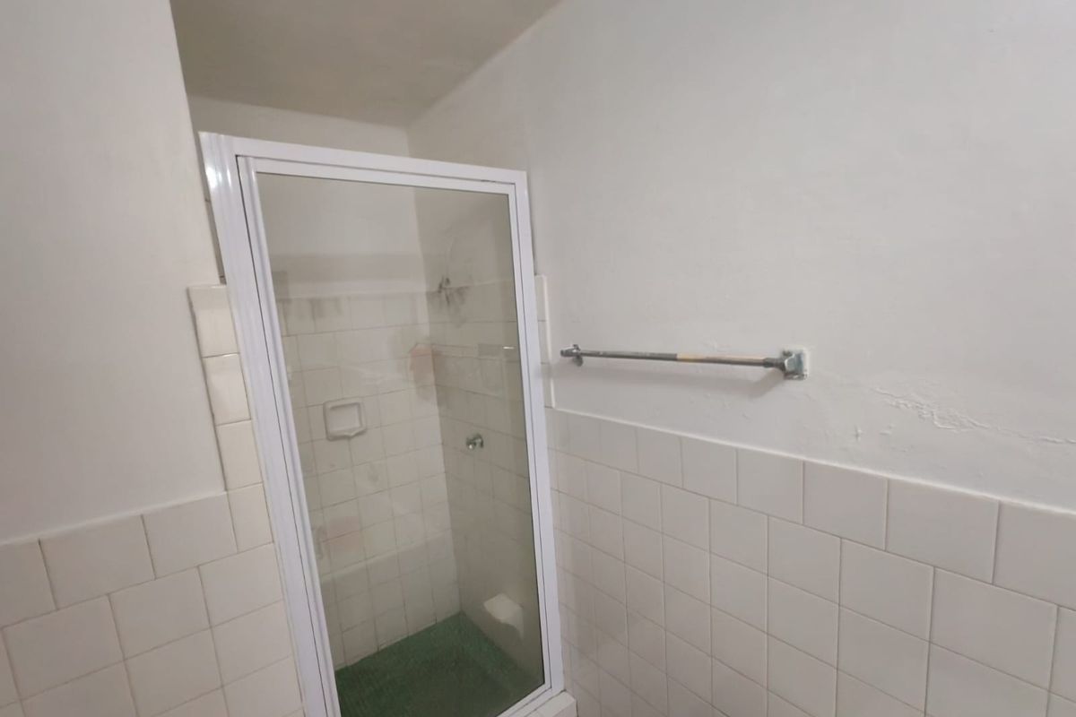 A functional bathroom featuring a shower enclosure with tiled walls and a wall-mounted towel rail, requiring minor cosmetic updates.