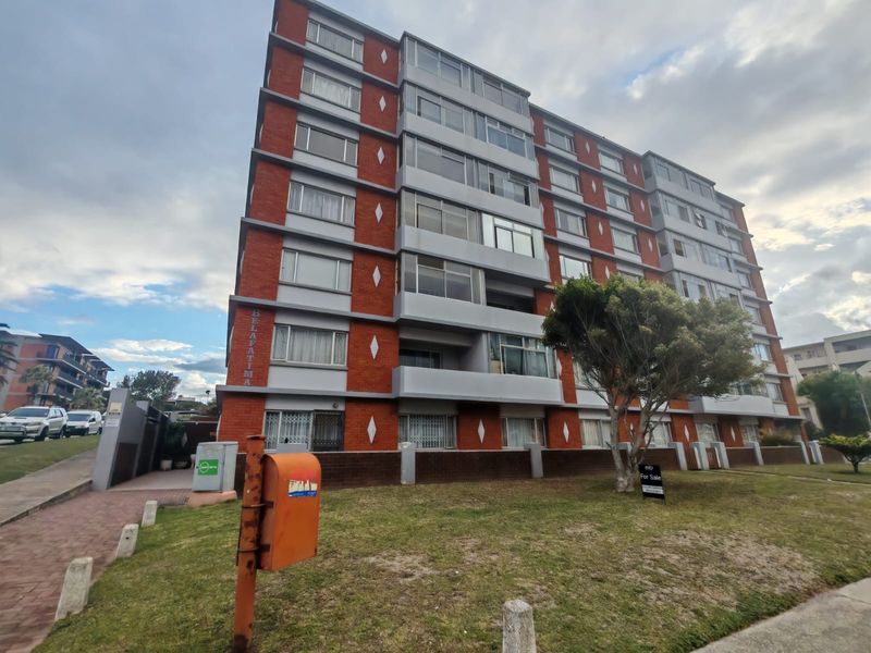 Exterior view of the Belafatma apartment complex, featuring a multi-story brick facade with enclosed balconies and a paved entrance area.