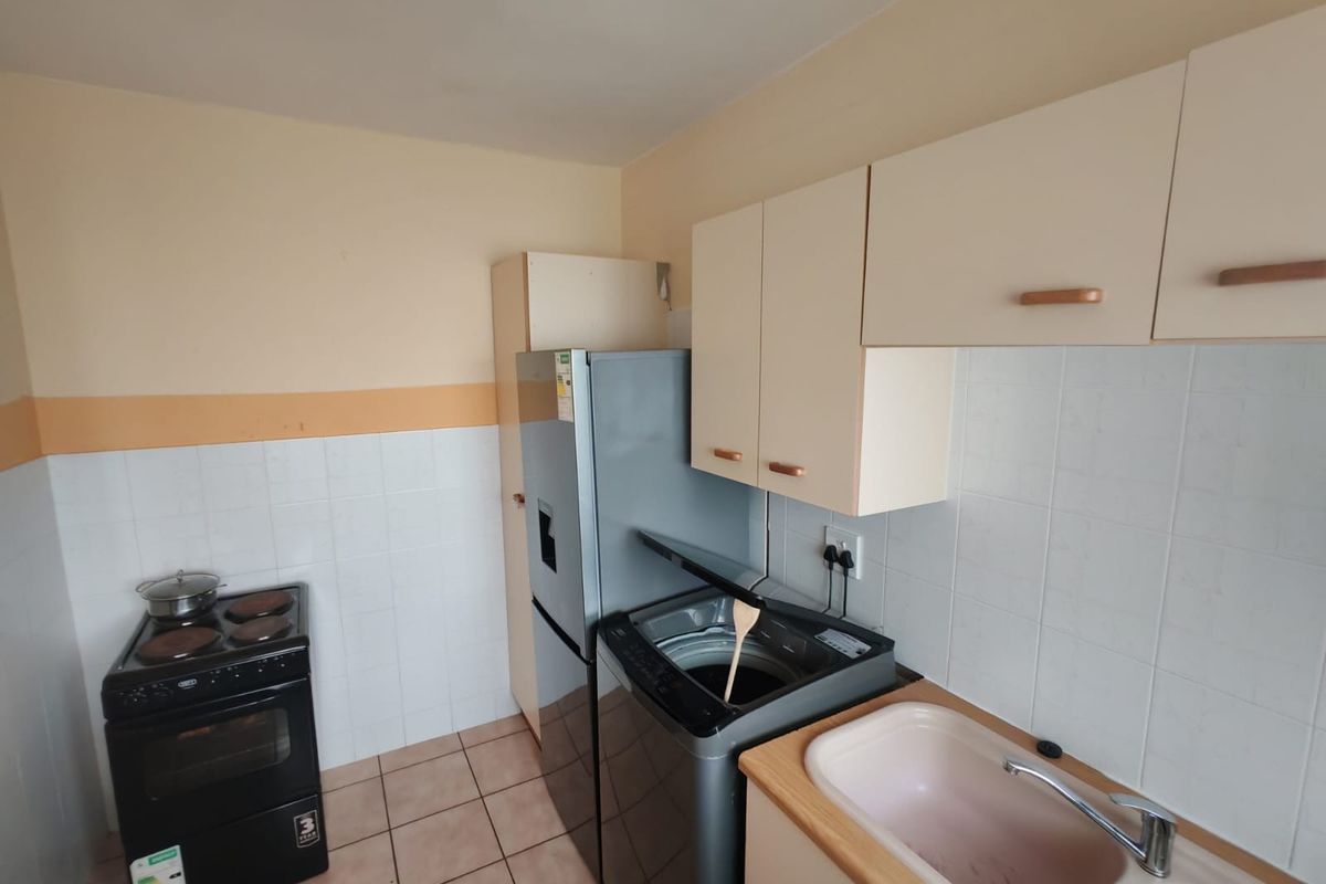 Compact kitchen featuring tiled splashbacks, built-in cabinetry, a sink, and a freestanding stove, offering a functional layout for daily use.