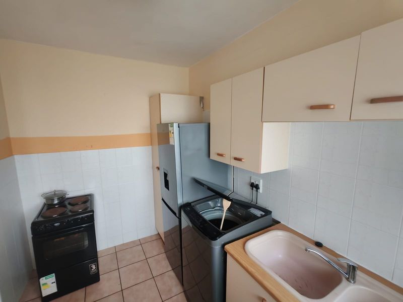 Compact kitchen featuring tiled splashbacks, built-in cabinetry, a sink, and a freestanding stove, offering a functional layout for daily use.