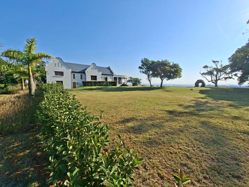 A spacious rear garden featuring a well-maintained lawn and a white gabled residential building with a covered patio area.