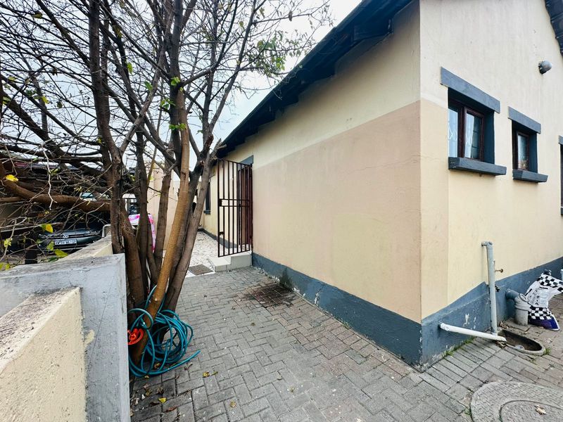 A side view of the property showing a paved walkway, security gate, and exterior wall finishes requiring maintenance.