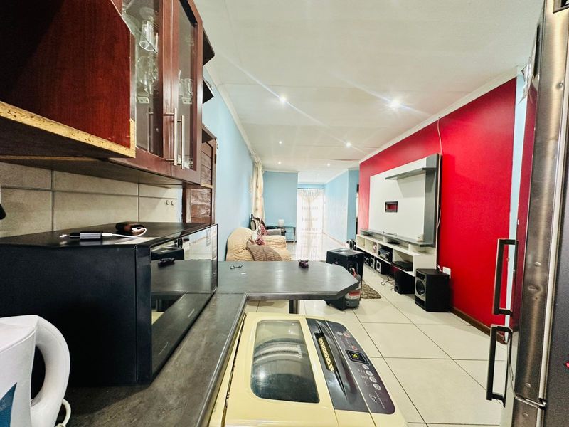 Open-plan living and kitchen area featuring tiled flooring, recessed lighting, and a built-in media wall with bold accent paint.