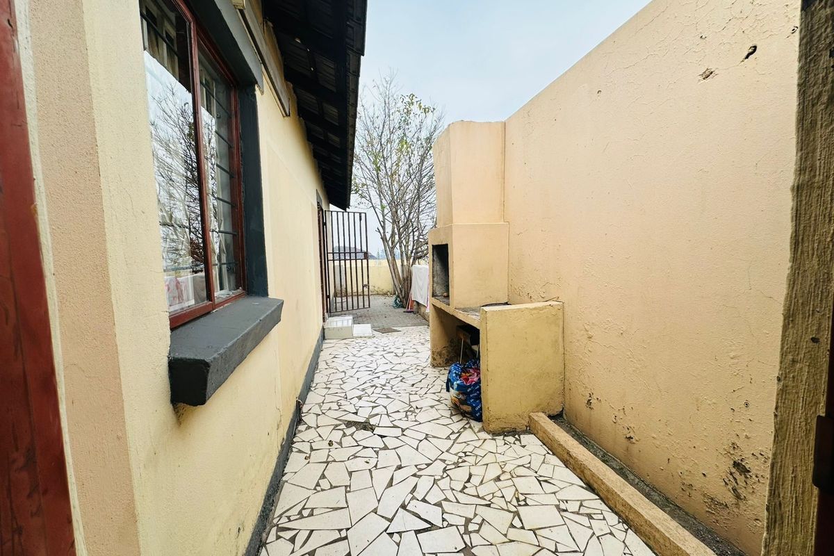 Outdoor patio area featuring a built-in braai, tiled flooring, and direct access to the rear garden area.