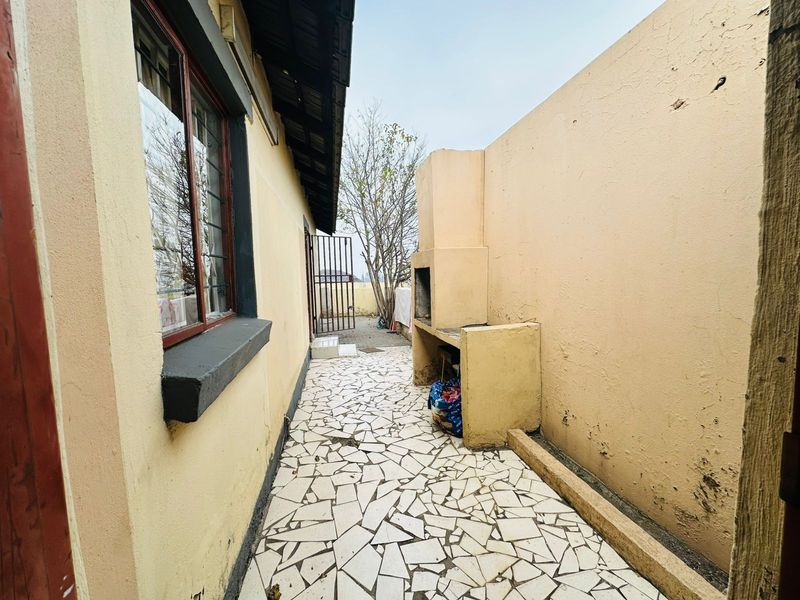 Outdoor patio area featuring a built-in braai, tiled flooring, and direct access to the rear garden area.