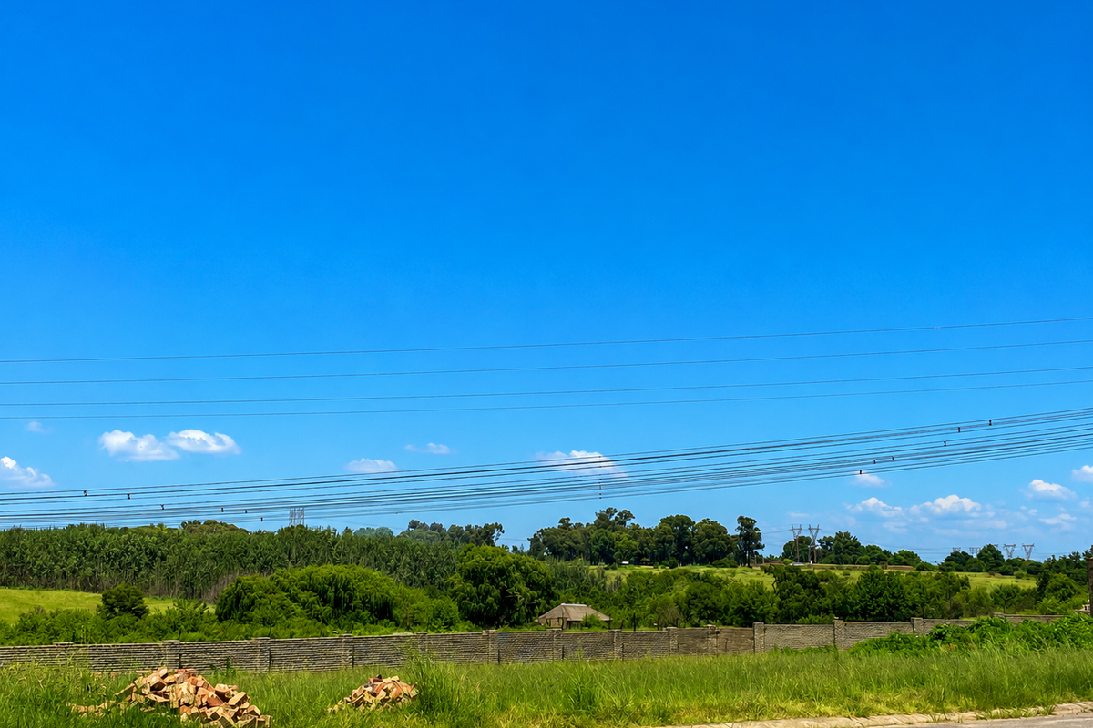 A view of the vacant residential land featuring a boundary wall, surrounding greenery, and overhead power lines against a clear blue sky.