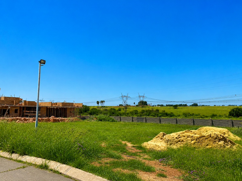 A vacant residential plot featuring a boundary wall, street lighting, and construction debris, situated in an open development area.