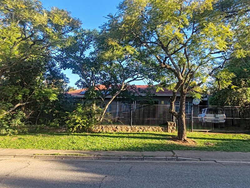 Front view of a residential property featuring a stone boundary wall, metal security fencing, and mature trees providing privacy from the street.