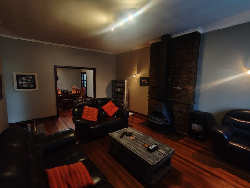 Spacious living room featuring a prominent stone fireplace, rich hardwood flooring, and warm ambient lighting, with an open transition to the adjacent dining area.