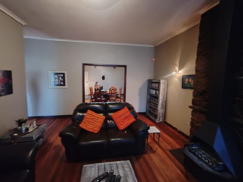 Living room featuring polished hardwood flooring and a prominent stone fireplace, with an open transition to the adjacent dining area.
