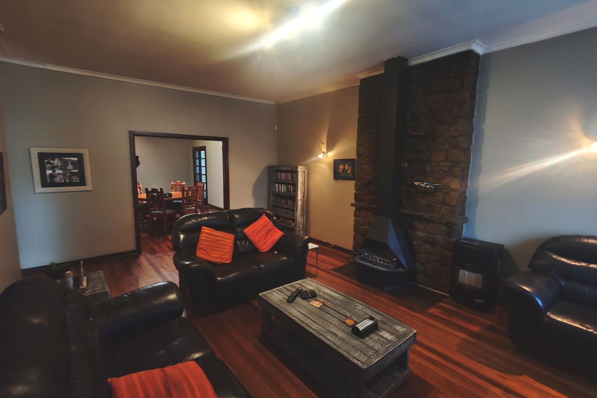 A living room featuring a prominent stone fireplace, hardwood flooring, and coving, with an open transition to the adjacent dining area.