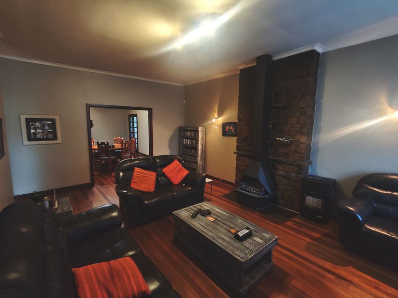 A living room featuring a prominent stone fireplace, hardwood flooring, and coving, with an open transition to the adjacent dining area.