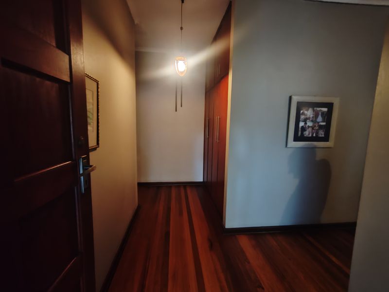 A well-maintained hallway featuring rich hardwood flooring, built-in wooden cabinetry, and a central pendant light fixture.