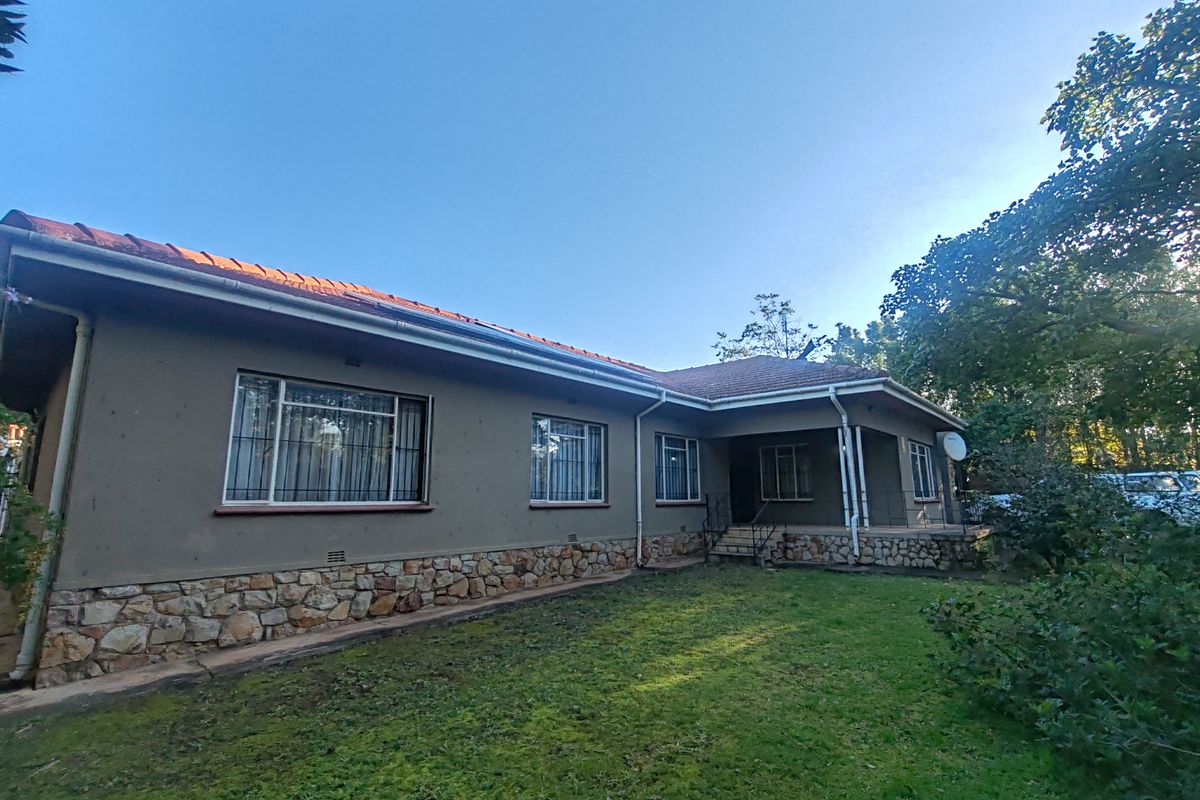 Rear view of the house featuring stone cladding, a covered patio area, and a spacious garden.