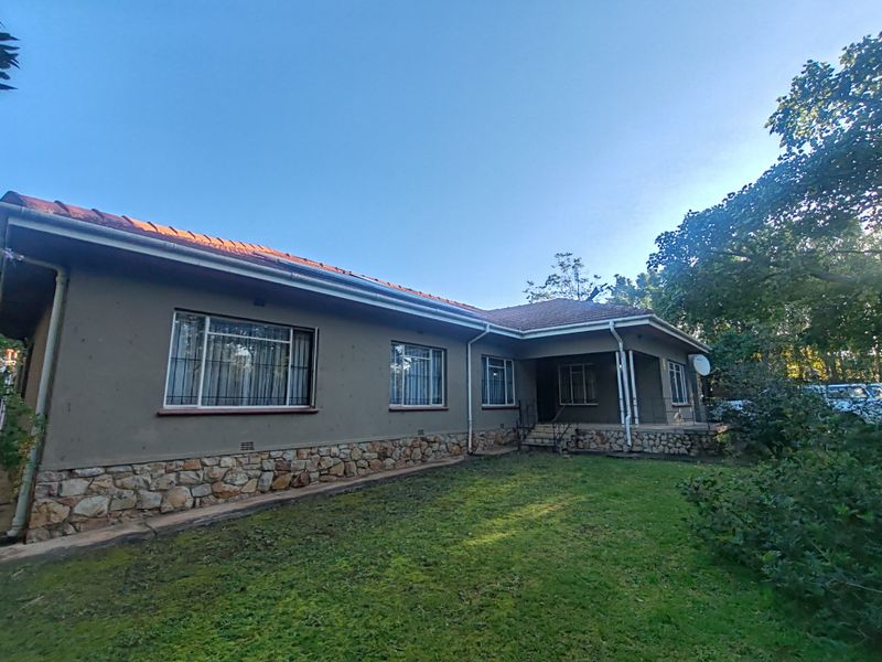 Rear view of the house featuring stone cladding, a covered patio area, and a spacious garden.