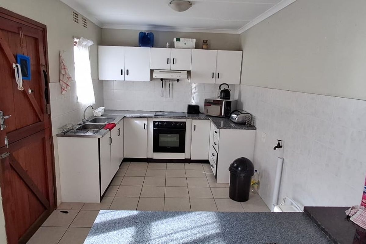 Functional kitchen featuring white built-in cabinetry, laminate countertops, integrated oven and hob, and tiled splashbacks with direct access to an exterior door.