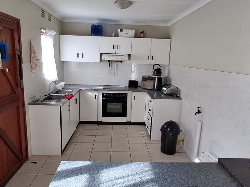 Functional kitchen featuring white built-in cabinetry, laminate countertops, integrated oven and hob, and tiled splashbacks with direct access to an exterior door.