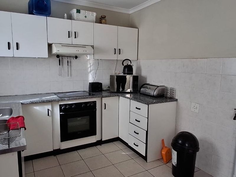 A functional kitchen featuring white cabinetry, laminate countertops, a built-in oven with extractor fan, and tiled splashbacks.
